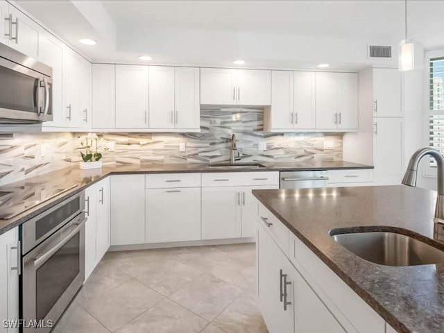 kitchen with dark stone countertops, visible vents, appliances with stainless steel finishes, and a sink