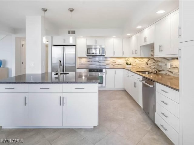 kitchen with an island with sink, decorative backsplash, stainless steel appliances, white cabinetry, and a sink