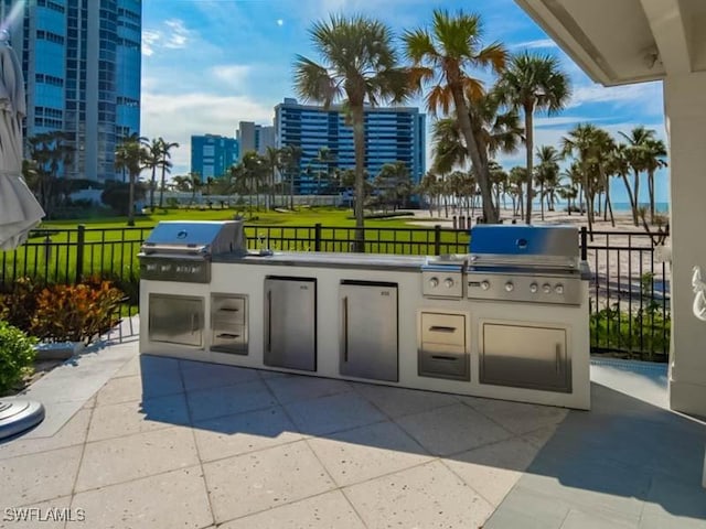 view of patio with fence, grilling area, a city view, and exterior kitchen