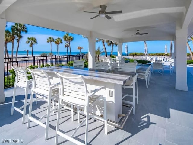 view of patio featuring fence, ceiling fan, outdoor dry bar, and a water view