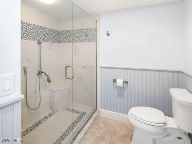 bathroom featuring a wainscoted wall, toilet, and a shower stall