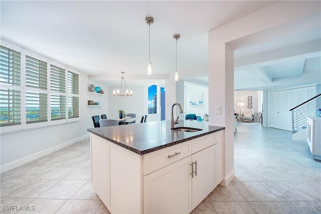 kitchen featuring dark stone countertops, a sink, an inviting chandelier, pendant lighting, and baseboards