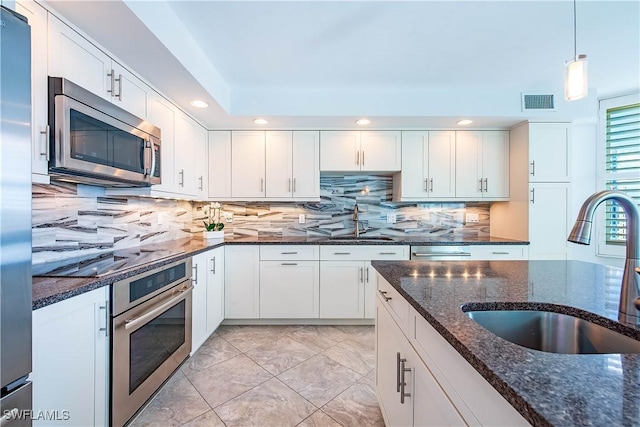 kitchen with dark stone countertops, a sink, stainless steel appliances, backsplash, and white cabinetry