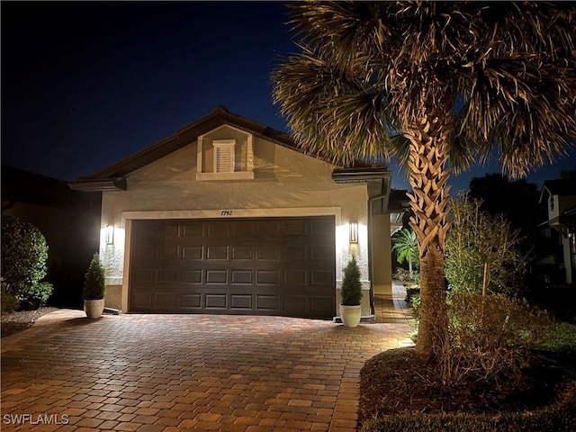 view of front of house with stucco siding, decorative driveway, and an attached garage