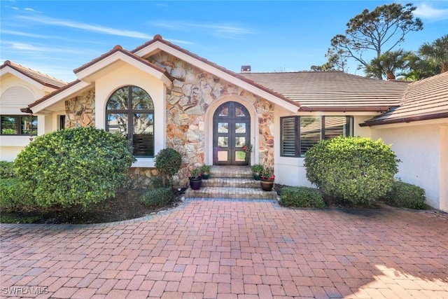 doorway to property with a tiled roof, french doors, stone siding, and stucco siding