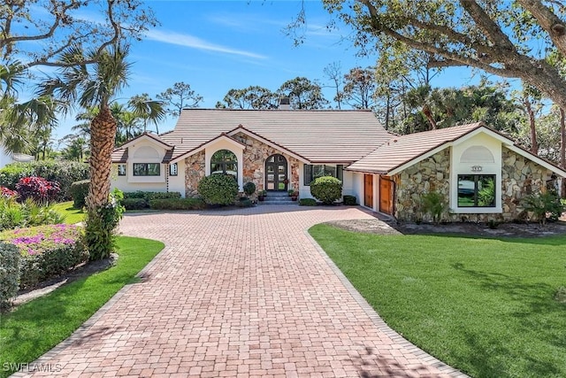 view of front of property with stone siding, a tiled roof, decorative driveway, and a front lawn