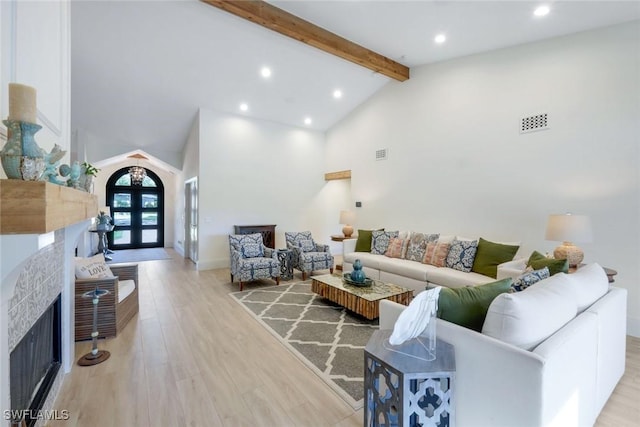 living area with visible vents, beamed ceiling, a fireplace, light wood-style floors, and arched walkways