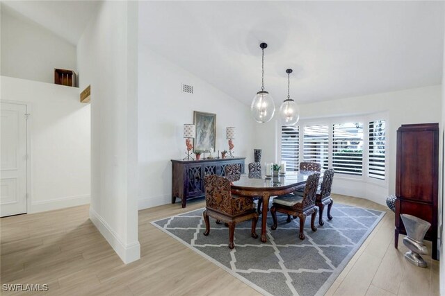 dining room with visible vents, baseboards, light wood-style floors, and high vaulted ceiling