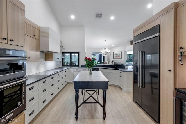 kitchen featuring dark countertops, visible vents, multiple ovens, built in refrigerator, and a peninsula