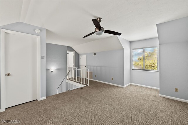 carpeted spare room with vaulted ceiling, visible vents, baseboards, and ceiling fan