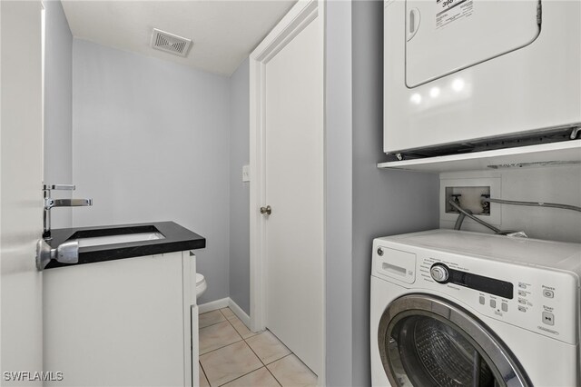 washroom with visible vents, laundry area, light tile patterned flooring, a sink, and stacked washer and dryer