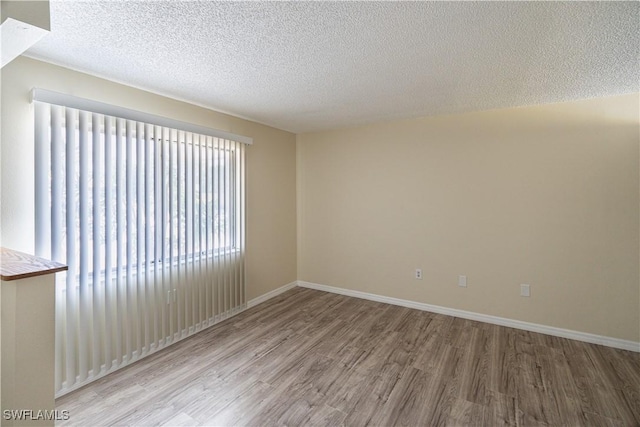 spare room with a textured ceiling, baseboards, and wood finished floors