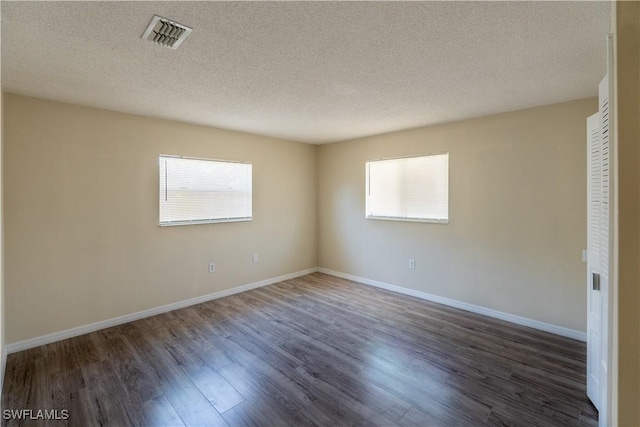 empty room featuring visible vents, baseboards, a textured ceiling, and wood finished floors