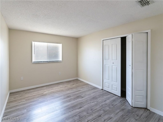 unfurnished bedroom featuring a closet, visible vents, baseboards, and wood finished floors