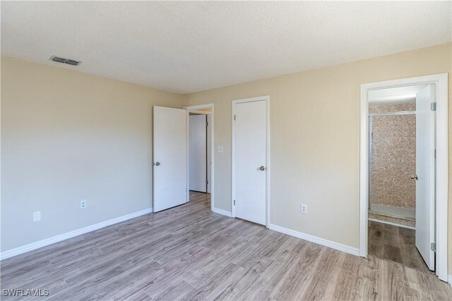 unfurnished bedroom featuring visible vents, baseboards, a textured ceiling, and light wood-style flooring