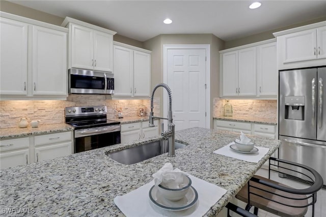 kitchen featuring a sink, a kitchen breakfast bar, backsplash, white cabinetry, and appliances with stainless steel finishes