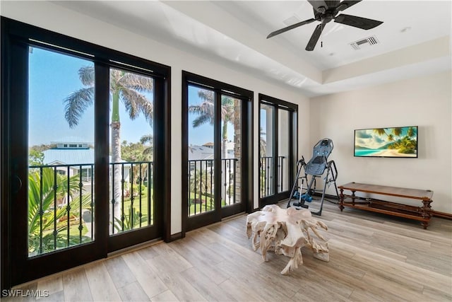 exercise room featuring visible vents, baseboards, a tray ceiling, wood finished floors, and a ceiling fan