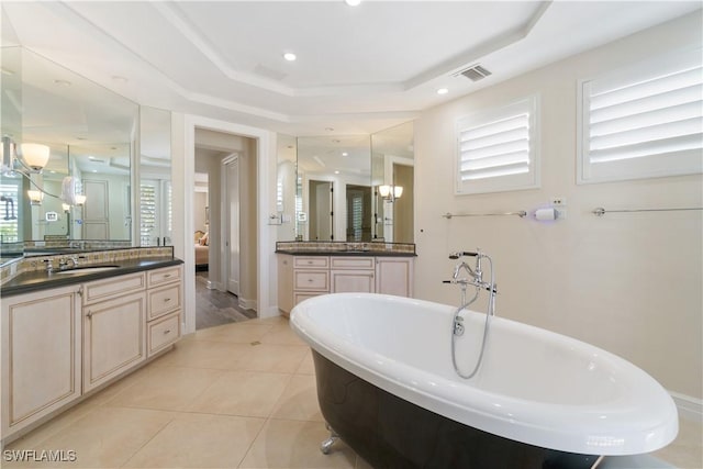 full bath featuring tile patterned flooring, visible vents, a tray ceiling, a freestanding tub, and a sink