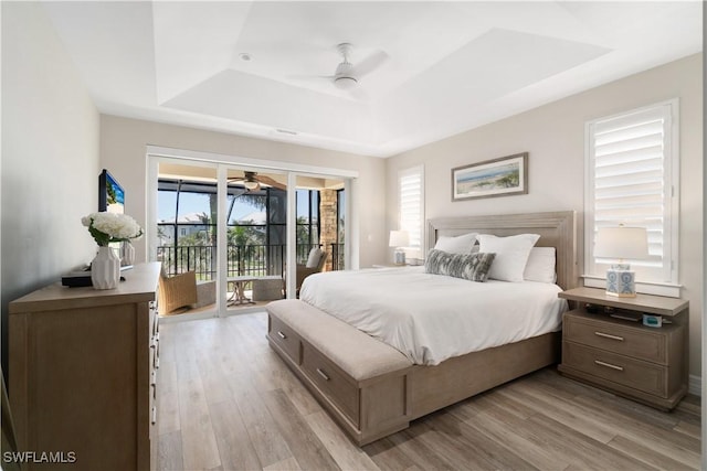 bedroom with light wood-style flooring, a raised ceiling, access to exterior, and a ceiling fan