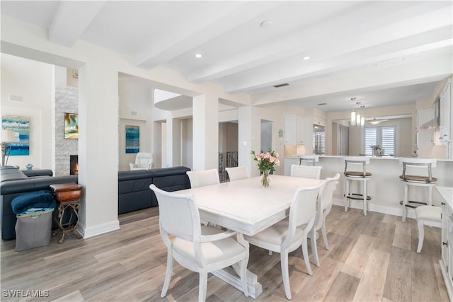 dining area with visible vents, baseboards, a stone fireplace, light wood-style floors, and beamed ceiling