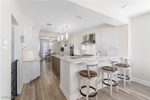 kitchen featuring visible vents, white cabinets, light wood-style floors, and wall chimney range hood