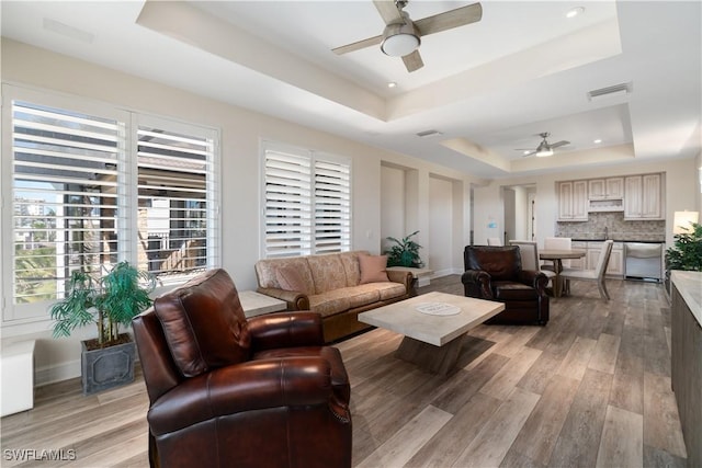 living area featuring light wood finished floors, visible vents, baseboards, ceiling fan, and a raised ceiling