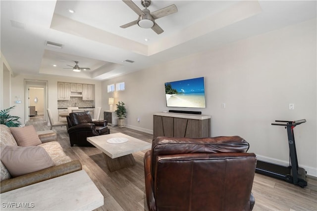 living room featuring a raised ceiling, baseboards, light wood-type flooring, and ceiling fan