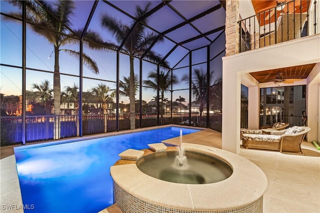 pool at dusk featuring glass enclosure, a pool with connected hot tub, and a patio