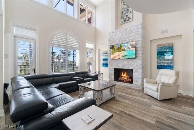 living area with light wood-type flooring, visible vents, a high ceiling, a fireplace, and baseboards