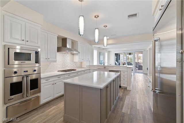 kitchen featuring a peninsula, a sink, built in appliances, a warming drawer, and wall chimney exhaust hood