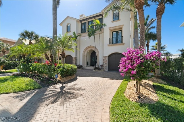 mediterranean / spanish-style house with a balcony, decorative driveway, stone siding, and stucco siding