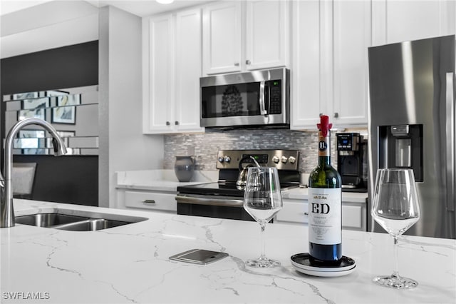 kitchen featuring backsplash, white cabinetry, stainless steel appliances, and a sink