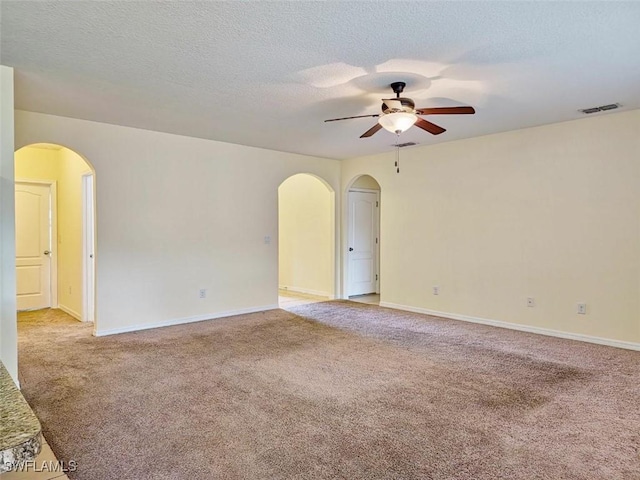 empty room with visible vents, arched walkways, light colored carpet, and a ceiling fan