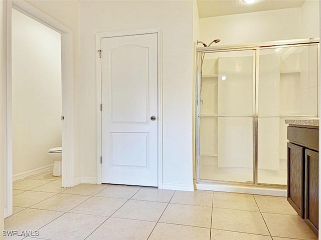 bathroom with baseboards, toilet, a stall shower, and tile patterned flooring