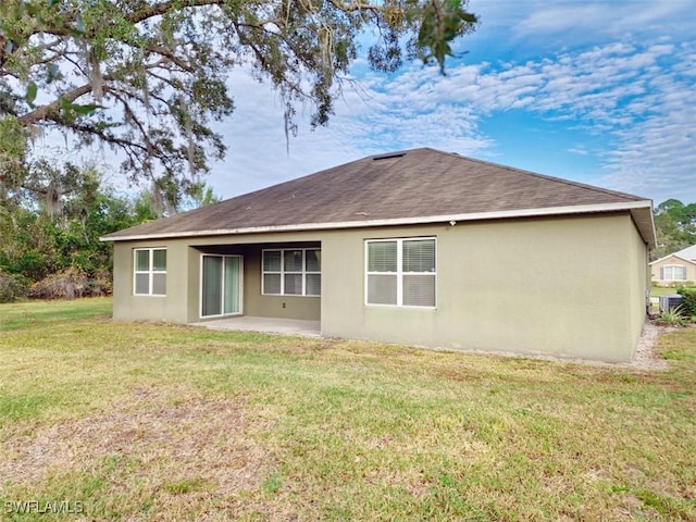 back of property with a yard, stucco siding, a patio, and roof with shingles