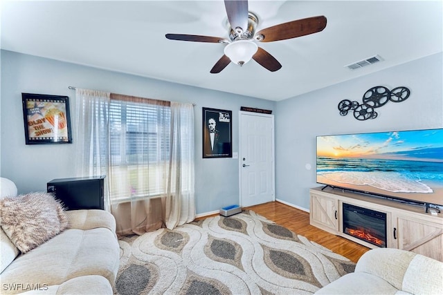 living area featuring ceiling fan, wood finished floors, visible vents, and baseboards