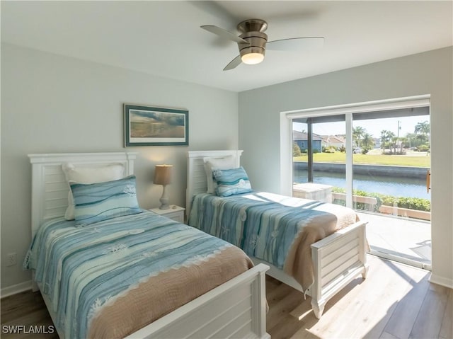 bedroom featuring access to exterior, wood finished floors, a water view, and baseboards