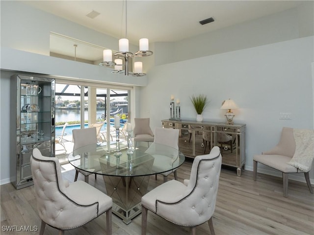 dining area with light wood finished floors, visible vents, a chandelier, and baseboards