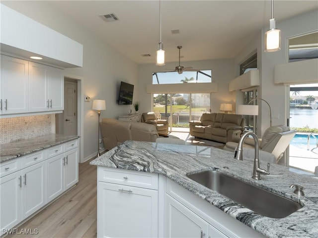 kitchen with a sink, open floor plan, white cabinets, light wood finished floors, and hanging light fixtures