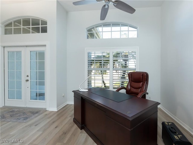 office featuring baseboards, ceiling fan, light wood-style flooring, french doors, and a high ceiling