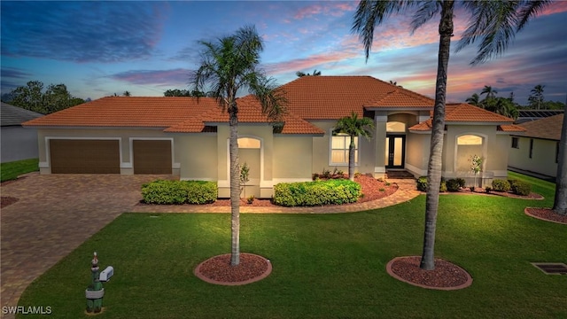 mediterranean / spanish home featuring an attached garage, a yard, stucco siding, a tile roof, and decorative driveway