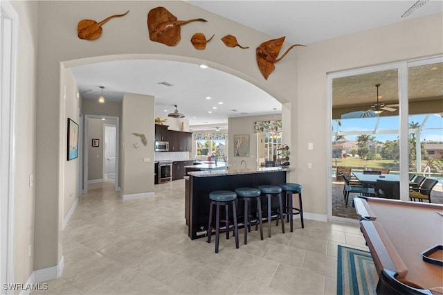 kitchen featuring dark brown cabinetry, a breakfast bar area, arched walkways, stainless steel appliances, and a ceiling fan