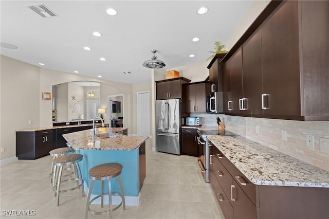 kitchen featuring tasteful backsplash, light stone countertops, appliances with stainless steel finishes, a kitchen breakfast bar, and arched walkways