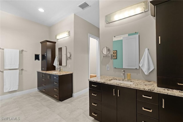 bathroom featuring visible vents, two vanities, baseboards, and a sink