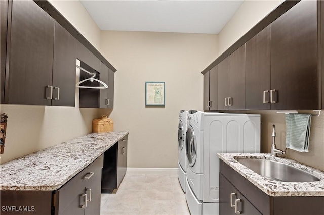 washroom with a sink, washer and dryer, cabinet space, light tile patterned floors, and baseboards