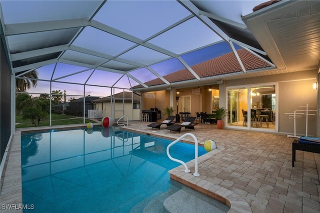 pool at dusk featuring a shed, glass enclosure, an outdoor structure, an outdoor pool, and a patio