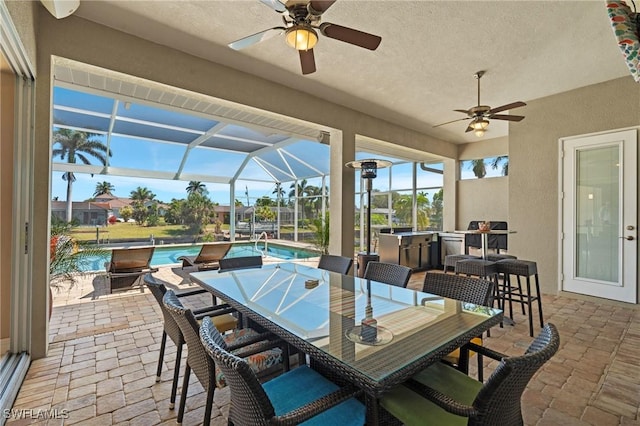 view of patio / terrace featuring a lanai, an outdoor pool, exterior kitchen, and a ceiling fan