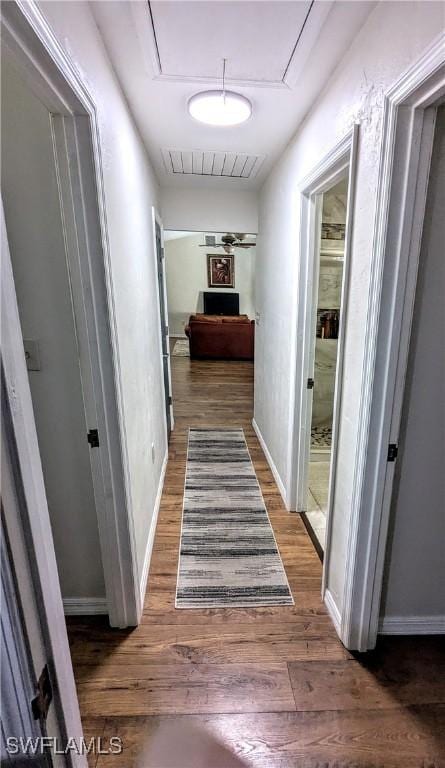 hall featuring attic access, wood finished floors, visible vents, and baseboards