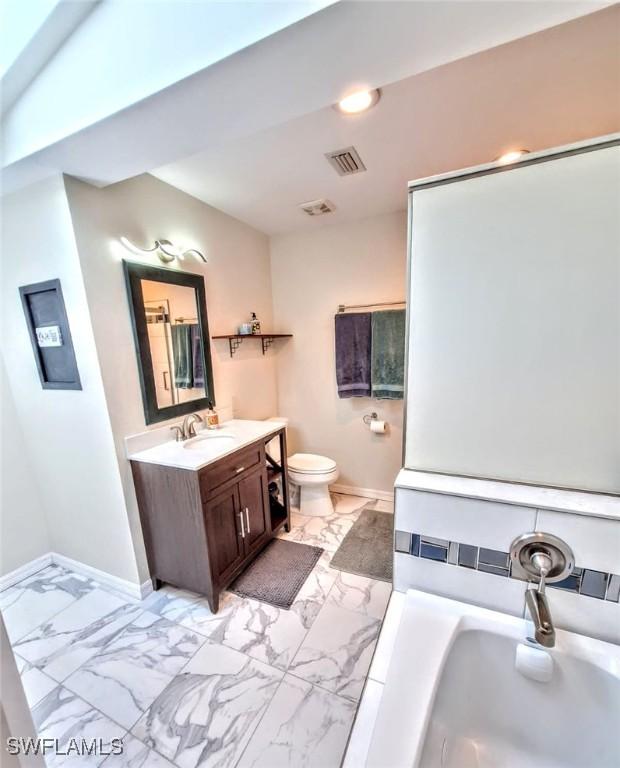 bathroom with baseboards, toilet, a tub to relax in, and marble finish floor