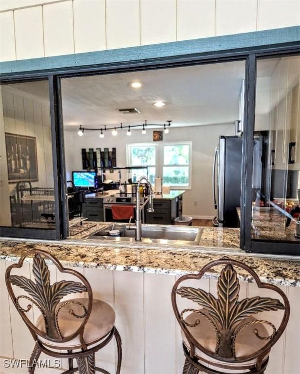 kitchen featuring light stone countertops, a sink, a breakfast bar, white cabinetry, and freestanding refrigerator
